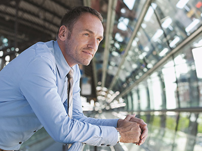 Business man leaning on a railing looking outside