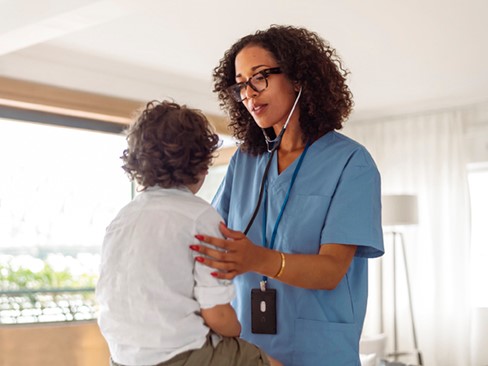 A black female doctor uses a stethoscope to check the lungs of a pediatric patient during a medical appointment.