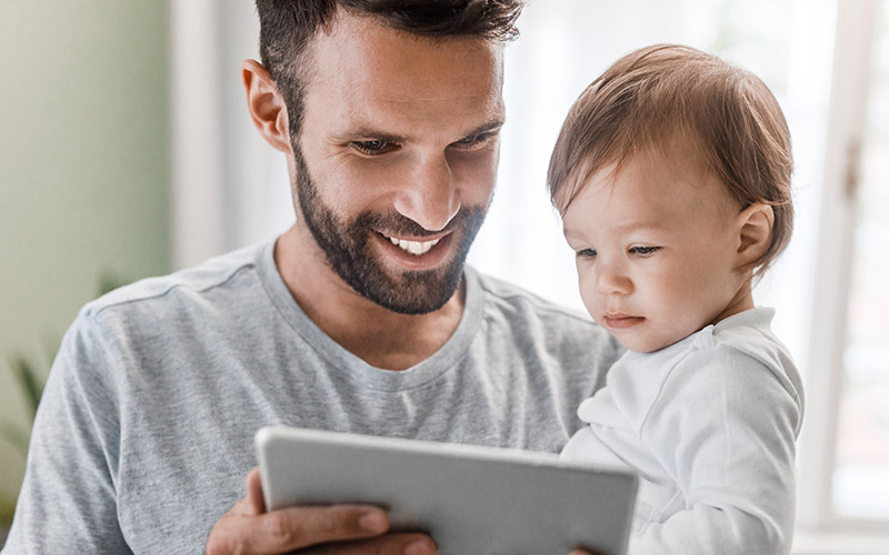 Father holding baby looking at a tablet